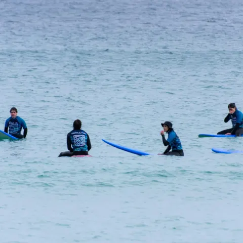 Groupe de surfeurs en combinaison, assis sur leurs planches dans l'eau