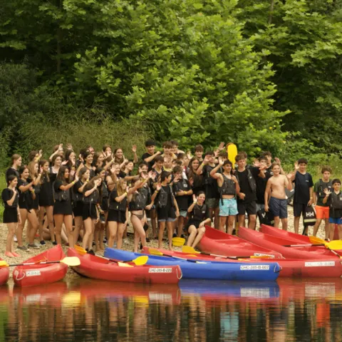 Grand groupe posant devant des kayaks sur la berge d'une rivière
