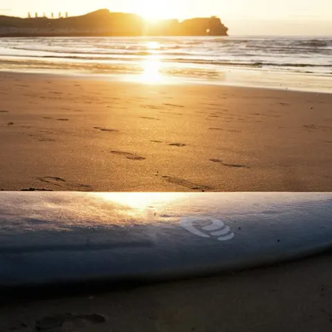 Planche de surf sur le sable au coucher du soleil