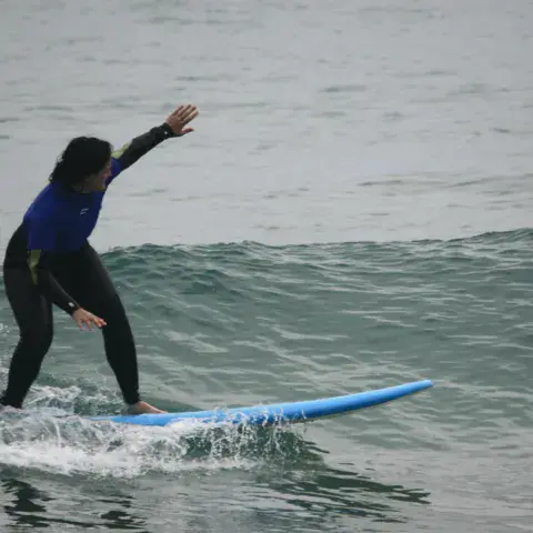 Élève de surf debout sur une planche bleue