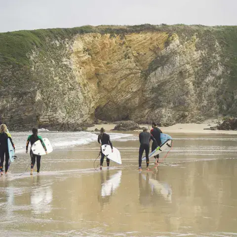 Élèves rejoignant l'eau avec leurs planches au pied de la falaise