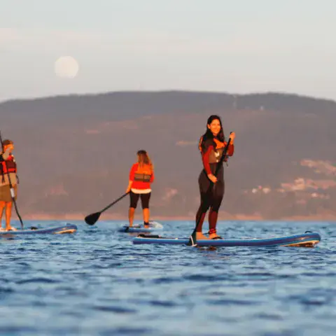 Pagayeuse debout sur sa planche au coucher du soleil