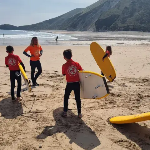 Élèves sur le sable avec leurs planches, montagne en arrière-plan