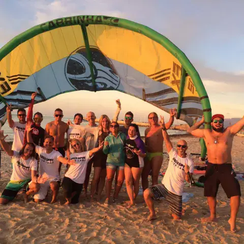 Groupe de kitesurfeurs sous une aile, sur la plage
