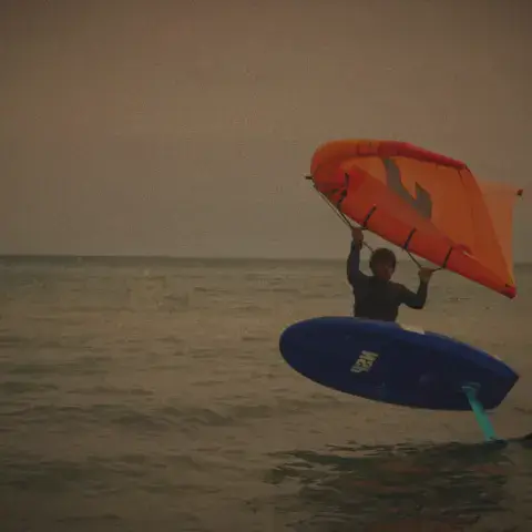 Rider de wing foil tenant son aile au-dessus de l'eau