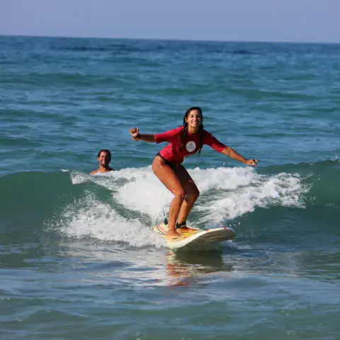 Surfeuse debout sur sa planche dans une vague