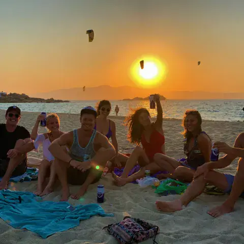 Groupe assis sur la plage au coucher du soleil, kites dans le ciel