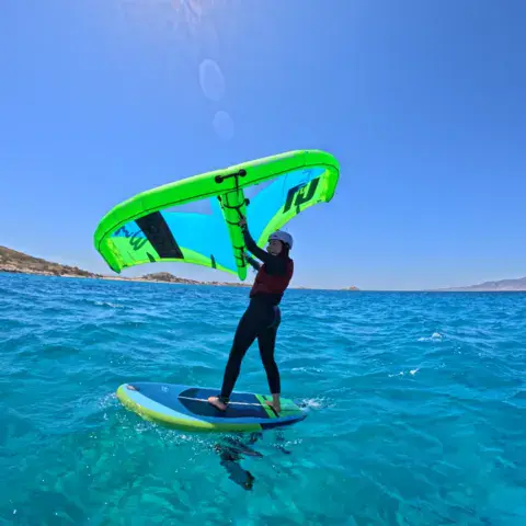 Rider de wingfoil debout sur sa planche, aile verte en main