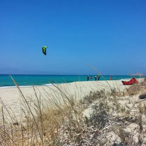 Plage de sable bordée de dunes, aile de kite dans le ciel