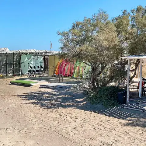 Station de windsurf sur la plage, voiles rangées sous les arbres
