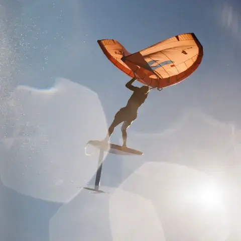 Wing foil, pratiquant vu de dessous avec son aile orange