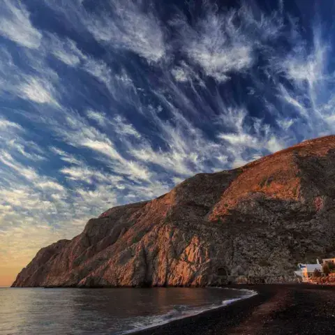 Falaise rocheuse et plage de sable noir au coucher du soleil