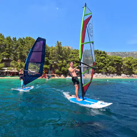 Deux planches à voile sur l'eau devant une plage bordée de pins