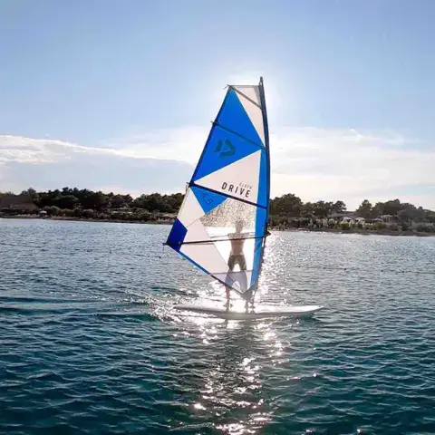 Windsurfeur sous voile bleue et blanche sur une eau calme