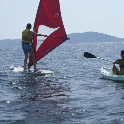 Planche à voile à voile rouge et paddlers sur une mer calme
