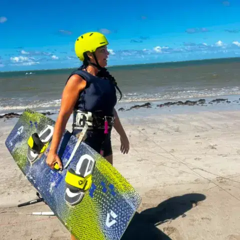 Élève portant sa planche sur le sable