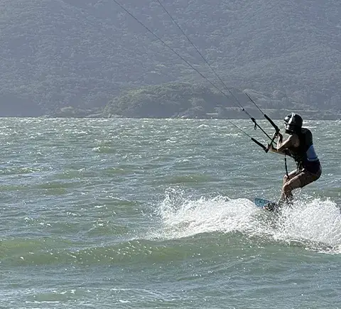 Kitesurfeur en navigation devant un relief boisé