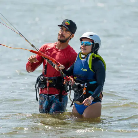 Deux élèves avec leur équipement de kitesurf au bord de l'eau