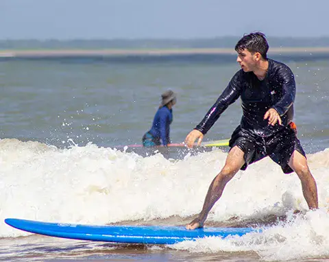 Élève debout sur une planche softboard bleue dans les vagues
