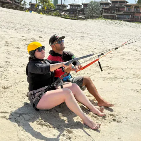 Exercice avec une barre de kite sur le sable, deux personnes assises