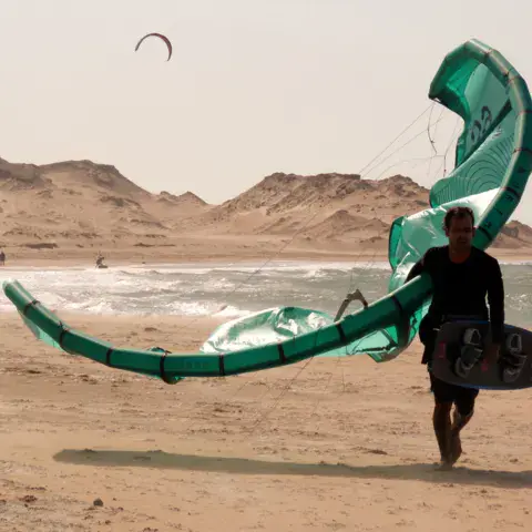 Kitesurfeur marchant sur la plage avec son kite et sa planche