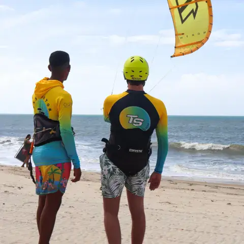 Deux personnes sur la plage face à un kite jaune dans le ciel
