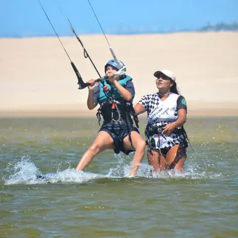 Deux kitesurfeurs dans l'eau peu profonde devant les dunes