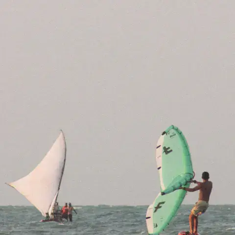 Wingfoiler sur l'eau à côté d'un bateau à voile latine