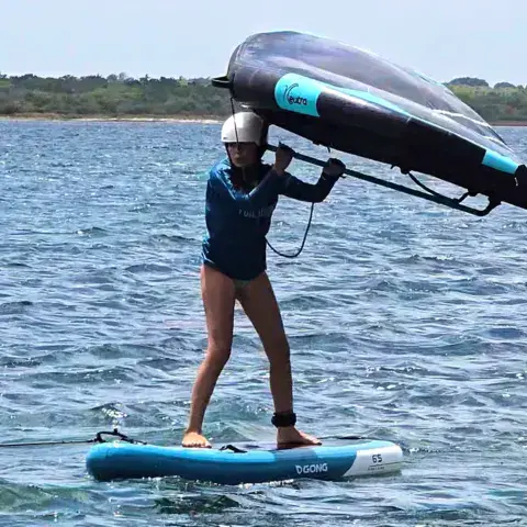 Wingfoiler debout sur sa planche, aile en main, sur une lagune