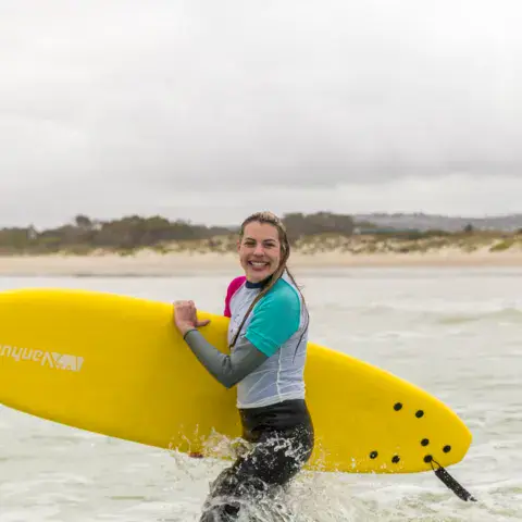 Surfeuse avec une planche jaune au bord de l'eau