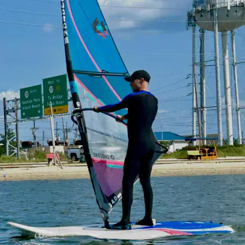 Windsurfeur debout sur sa planche près du bord, voile dressée