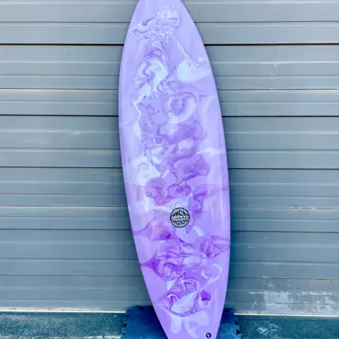 Planche de surf violette marbrée, adossée à un mur