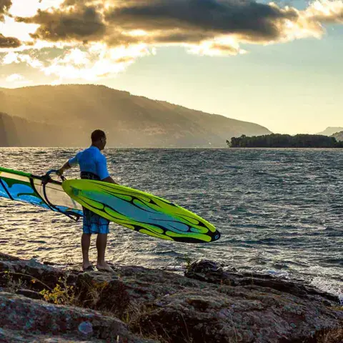 Windsurfeur avec sa planche et sa voile au bord de l'eau