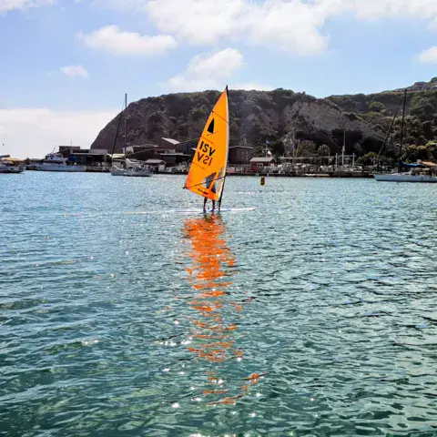 Windsurfeur avec une voile orange près d'un port