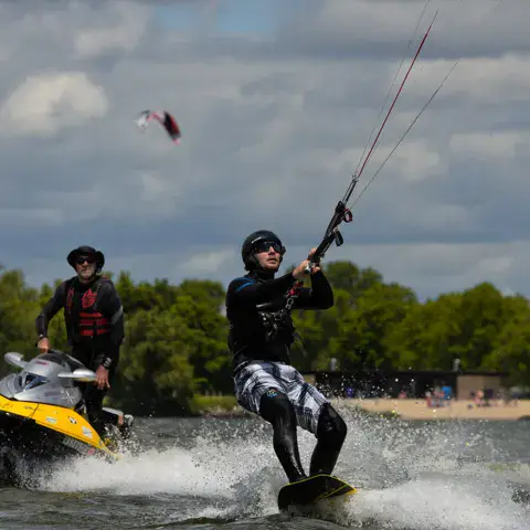 Rider de kite tracté sur l'eau, avec un moniteur en jet-ski derrière lui
