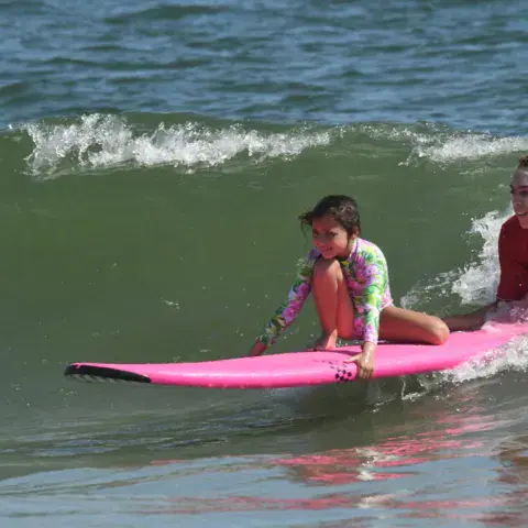 Moniteur accompagnant une enfant sur une planche rose dans les vagues