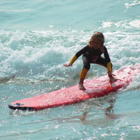 Jeune surfeuse en combinaison sur une planche rouge