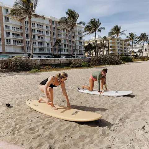 Exercices de départ sur planche, sur le sable d'une plage bordée de palmiers
