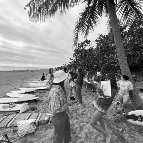 Groupe réuni sur la plage autour de planches, en noir et blanc