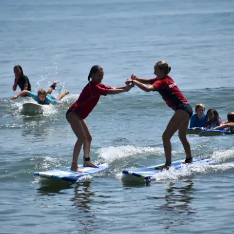 Deux enfants debout sur leurs planches dans les vagues pendant un cours