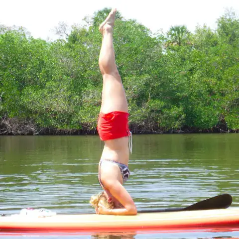 Pratiquante de paddle en équilibre sur la tête, sur une rivière bordée de mangrove