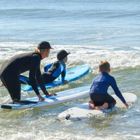 Cours de surf dans l'eau, avec des moniteurs et de jeunes élèves