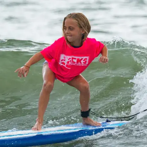 Jeune surfeuse en pleine vague sur une planche bleue