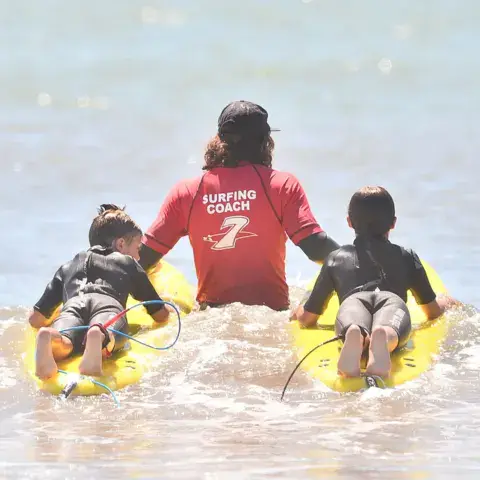 Un moniteur avec deux enfants sur des planches dans l'eau peu profonde