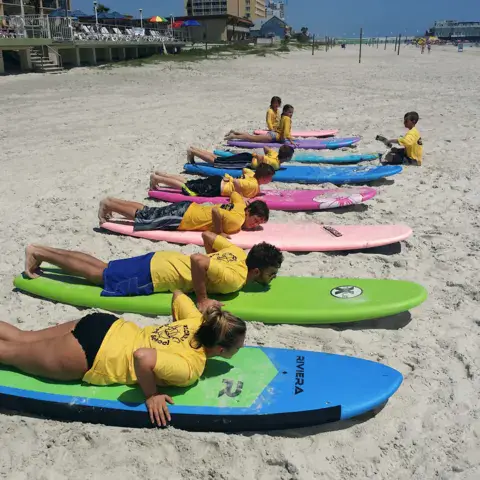 Élèves allongés sur leurs planches de surf sur la plage, pour un exercice de mise en place