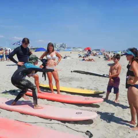 Un moniteur explique le lever sur la planche à un élève, sur le sable