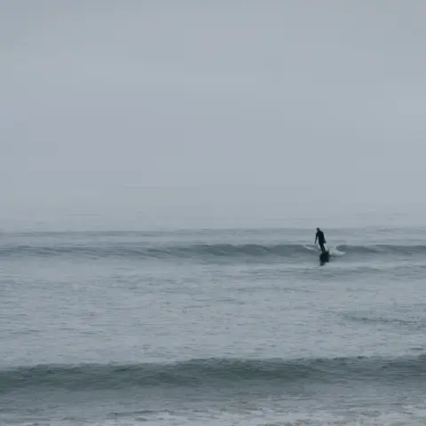 Un surfeur au large sur une petite vague, par temps brumeux