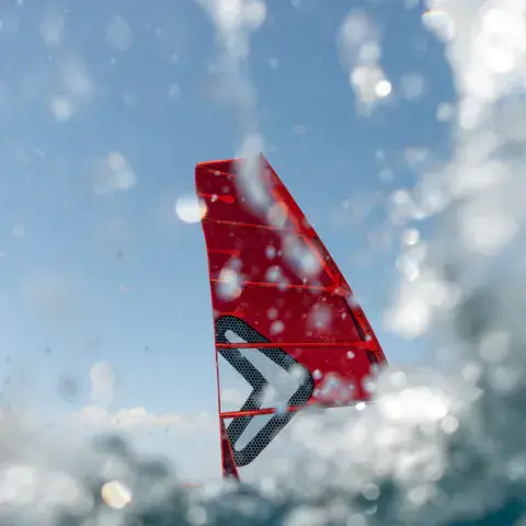 Voile de windsurf rouge en plein saut au-dessus de l'eau