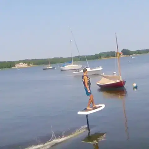 Rider en e-foil sur une baie, voiliers à l'arrière-plan