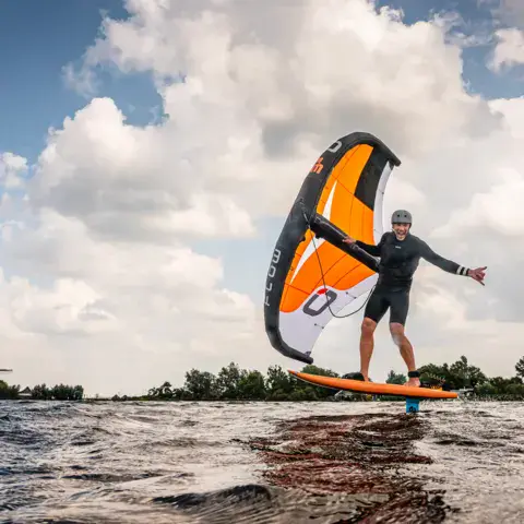 Rider de wing foil sur un plan d'eau intérieur, moulin à l'horizon